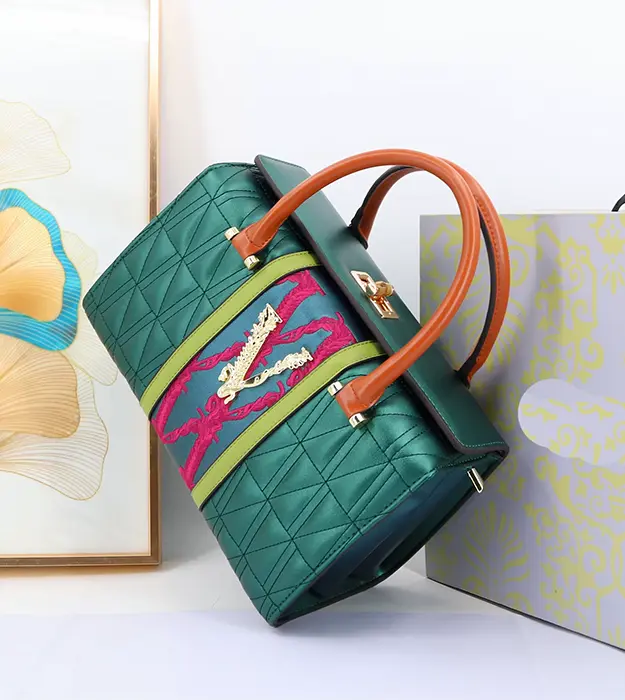 Elegantna zelena torba Auréva Chroméa sa zlatnim detaljima i ružičastim vezom, postavljena na svetloj pozadini