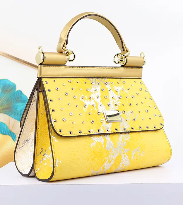 Elegantna ženska torba Luméa D’Or u žuto-zlatnoj boji sa dijamantskim detaljima i zlatnom drškom, postavljena na beloj pozadini.